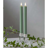 Zöld LED vacsoragyertyák dekor pohárban, meleg fényű lánggal, természetes zöld díszítéssel és elegáns hangulatban elrendezve.